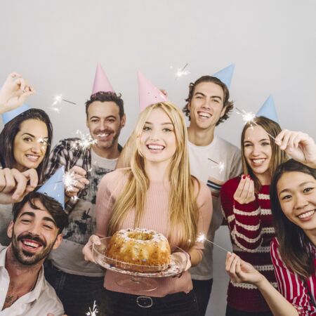 Das Bild zeigt eine Gruppe von Menschen (4 Frauen, 3 M&auml;nner, unterschiedlicher Nationalit&auml;ten und Aussehen) welche mit einem Kuchen und Sternenwerfer wohl Geburtstag feiern.